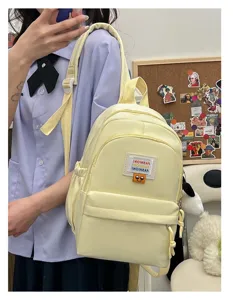 Vista dettagliata del mini zaino giallo con tasca frontale, cerniera e patch sorridente.
