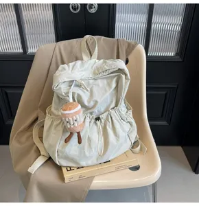 Detailed view of cream nylon backpack with cute plush charm, drawstring closure and casual style.