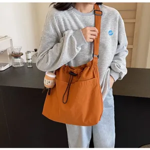 Detail view of casual orange canvas crossbody shoulder bag with drawstring and charm.