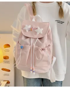 Detail view of the cute pink canvas backpack featuring fluffy star pendants and front pockets.