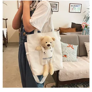 Vista detallada del bolso de lona lindo con osito de peluche y diseño de bolsillo frontal.