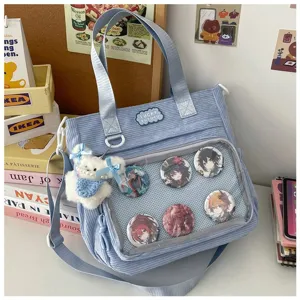 Gedetailleerd overzicht van blauwe corduroy ita tas met doorzichtig venster en anime badges.