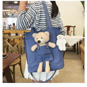Vista detallada del bolso cruzado de lona azul bonito con un peluche de oso y un colgante.