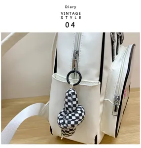 Vue détaillée d'un sac à dos en cuir PU blanc avec pendentif nœud à carreaux noir et blanc.
