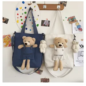 Detalle del bolso cruzado de lona con osito de peluche en el bolsillo y correa ajustable.