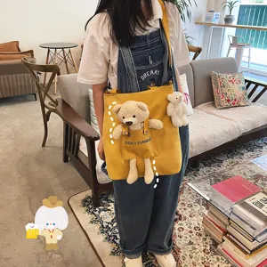 Toma detallada del bolso cruzado de lona amarilla con lindo oso de peluche y diseño de bolsillo.