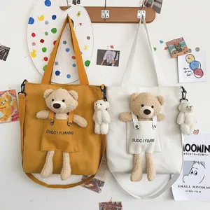 Detalle de bolso bandolera de lona lindo con colgante de muñeco de osito de peluche.