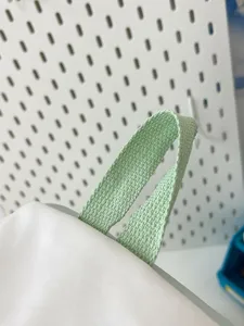 Close up view of light green woven strap detail for transparent doll backpack, fine fabric texture.