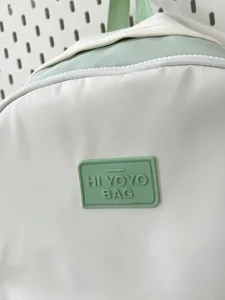 Japanese style backpack detail view white and green colorway with trendy rubber logo badge.