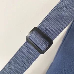 Detalle de la correa ajustable del bolso de lona, cinta de tela azul con hebilla negra.