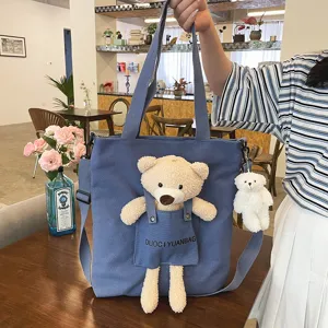 Bolso tote de lona azul con lindo colgante de oso de peluche y bolsillo frontal elegante.