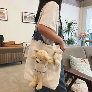Detalle del bolso de lona lindo con un osito de peluche y un llavero colgante pequeño.