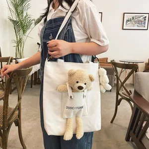 Vista detallada del bolso de lona lindo con colgante de oso de peluche y bolsillo frontal en cafetería.