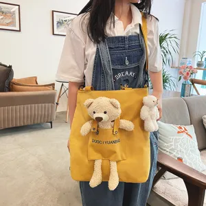Lindo bolso cruzado de lona amarilla con adorable colgante de muñeco y detalle de bolsillo
