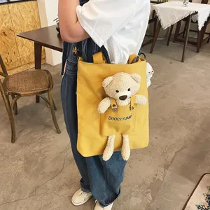 Vista detallada de bolso cruzado de lona amarilla con bonito bolsillo de peluche de oso.