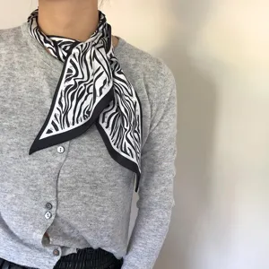 Detailansicht eines schmalen langen Seidenschals mit schwarz-weissem Zebramuster, Halsband.