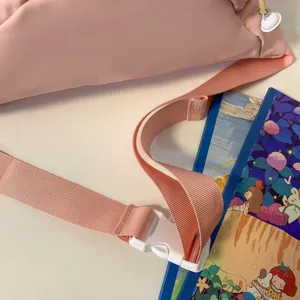 Gros plan sur les détails de la bandoulière en nylon rose et de la boucle en plastique blanc.