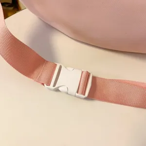 Gros plan detaille de la sangle de sac en nylon rose avec une boucle en plastique blanc.