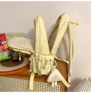 Detailed view of a light yellow canvas backpack featuring side pockets and a cute smile pendant.