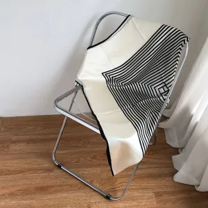 Gedetailleerd overzicht van een luxe zwart-witte geometrische zijden sjaal op een stoel.