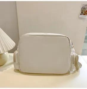 White crossbody shoulder bag detail view, featuring side zipper pockets and durable fabric.