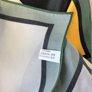 Close-up detail van luxe zijden vierkante sjaal met geometrisch kleurblok en zoom.