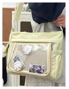 Vue détaillée du sac ita vert clair mignon avec une poche avant transparente et des badges.