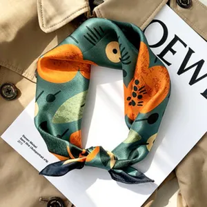 Close-up detail of luxury green silk scarf with abstract floral print and elegant rolled edges.