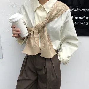 Detail shot of khaki knitted shoulder wrap shawl worn over white shirt for spring layering style.