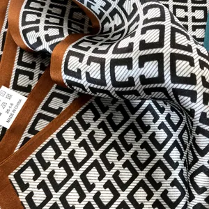 Détail de gros plan d'un foulard en satin de soie avec motif géométrique et bordure marron.