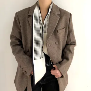 Vue détaillée d'un foulard étroit à pois noirs et blancs porté avec un blazer marron.