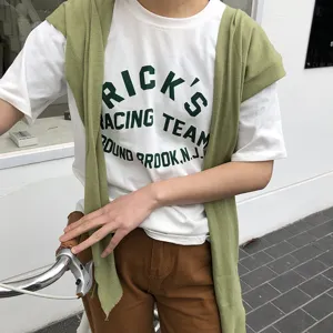 Vue de détail d'un t-shirt graphique blanc coréen avec un châle en tricot vert en extérieur.