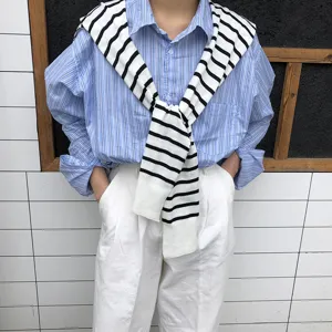 Vue détaillée de l'élégant châle en tricot rayé drapé sur une chemise rayée bleue.