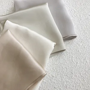 Silk scarf detail close-up showing soft smooth texture and elegant neutral color folding design.