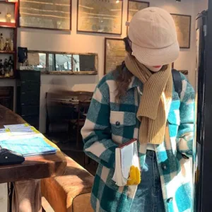 Detailansicht des warmen Strickschals und karierten Jackenoutfits in gemütlicher Café-Szene.
