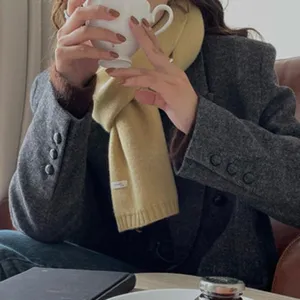 Detailaufnahme eines kuscheligen gelben Strickschals kombiniert mit einem grauen Blazer.