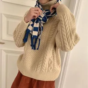 Detailansicht von kuscheligem Rollkragen-Zopfmuster-Pullover mit blau-weißem Karoschal.