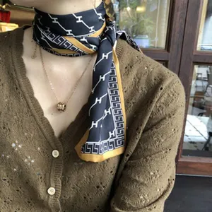 Gros plan détaillé du foulard en soie élégant au motif noir et doré porté gracieusement au cou.