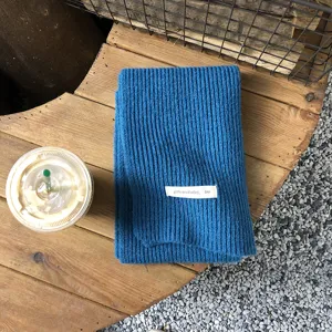 Detailaufnahme eines blauen Strickschals mit feiner Rippenstruktur und weißem Label.