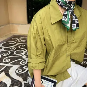 Chemise ample à manches longues verte associée à un détail de foulard en soie à carreaux.