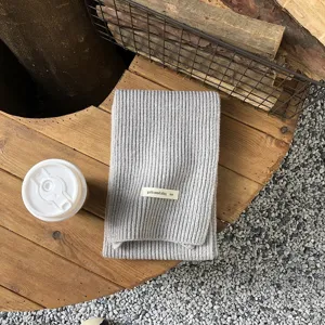 Grauer Strickschal Detail, gemütliche Wolle Textur Lifestyle flach auf Holztisch und Kies.