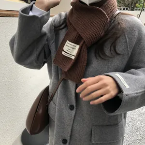 Nahaufnahme des braunen Strickschals mit stilvollem Stoffetikett und gemütlicher Textur.