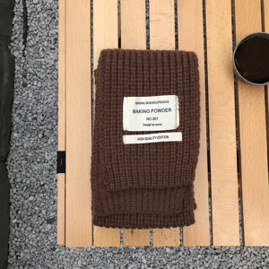Nahaufnahme des braunen Strickschals mit stilvollem Stoffetikett auf Holztisch und Kies.