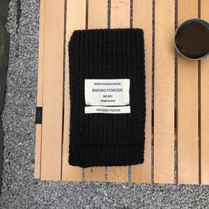 Detailaufnahme eines schwarzen Strickschals mit gewebtem Etikett auf Holztisch platziert.