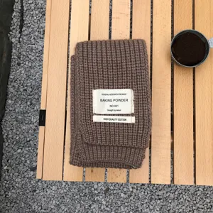 Brauner Strickschal für den Winter mit dekorativem Stoffetikett und gemütlicher Wollstruktur.