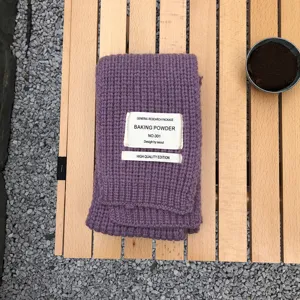 Nahaufnahme eines violetten, gestrickten Winterschals mit aufgenähtem Textiletikett.
