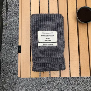Nahaufnahme eines dunkelgrauen Strickschals, ordentlich gefaltet auf Holzlatten mit Steinen.