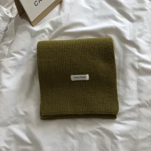 Vue en gros plan détaillée d'une écharpe d'hiver en tricot vert olive avec une petite étiquette.