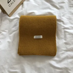 Vue rapprochée détaillée d'une écharpe d'hiver en tricot jaune moutarde avec petite étiquette.