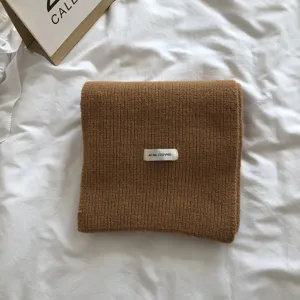 Vue détaillée d'un écharpe en tricot marron confortable pliée proprement sur lit blanc.